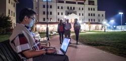 Student sitting on a bench with laptop at night